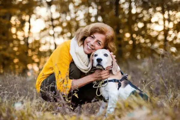 A happy senior woman with a dog on a walk in an autumn nature at sunset